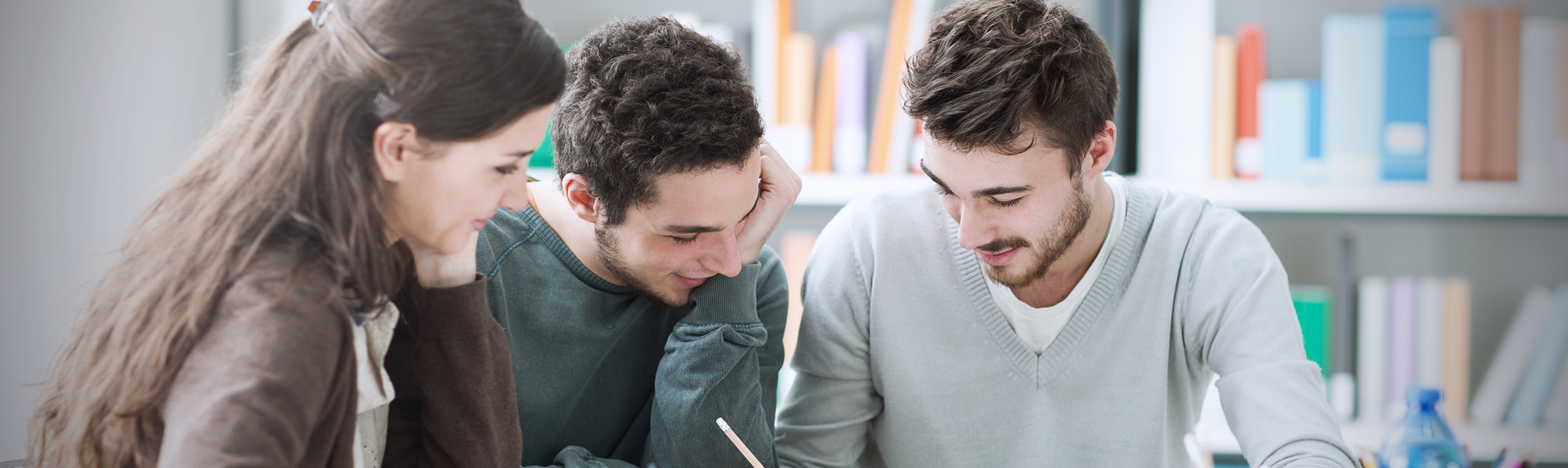 Tres estudiantes en una mesa de estudio de una biblioteca comparando sus apuntes